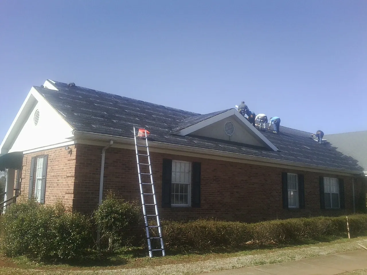 Crew tearing shingles off a brick ranch roof with a ladder set — Emergency Roof Repair work by our crew in New Milford