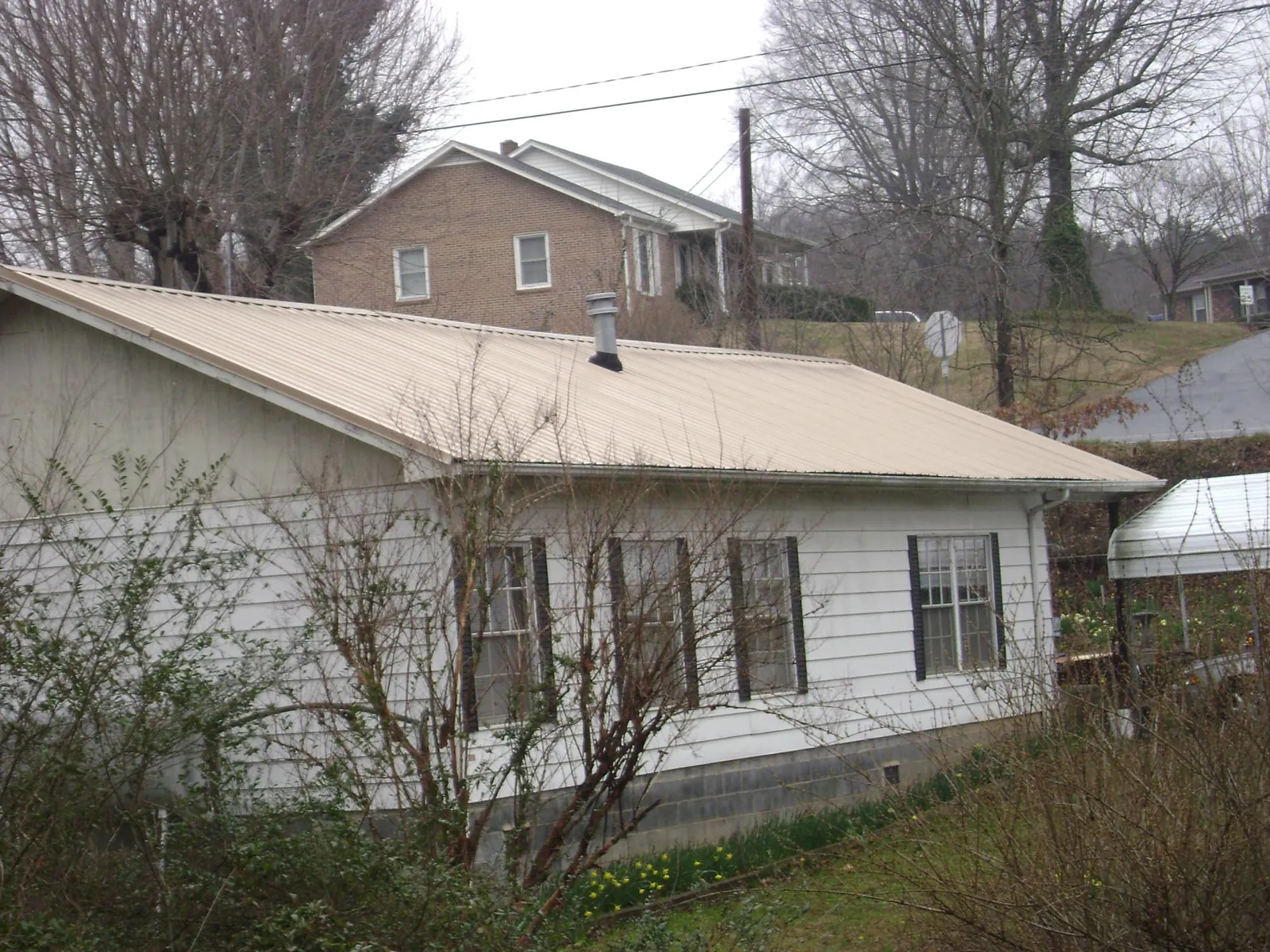 Tan metal roof on a white sided house set into a hillside — Commercial Roofing by Roofing Brothers in New Milford